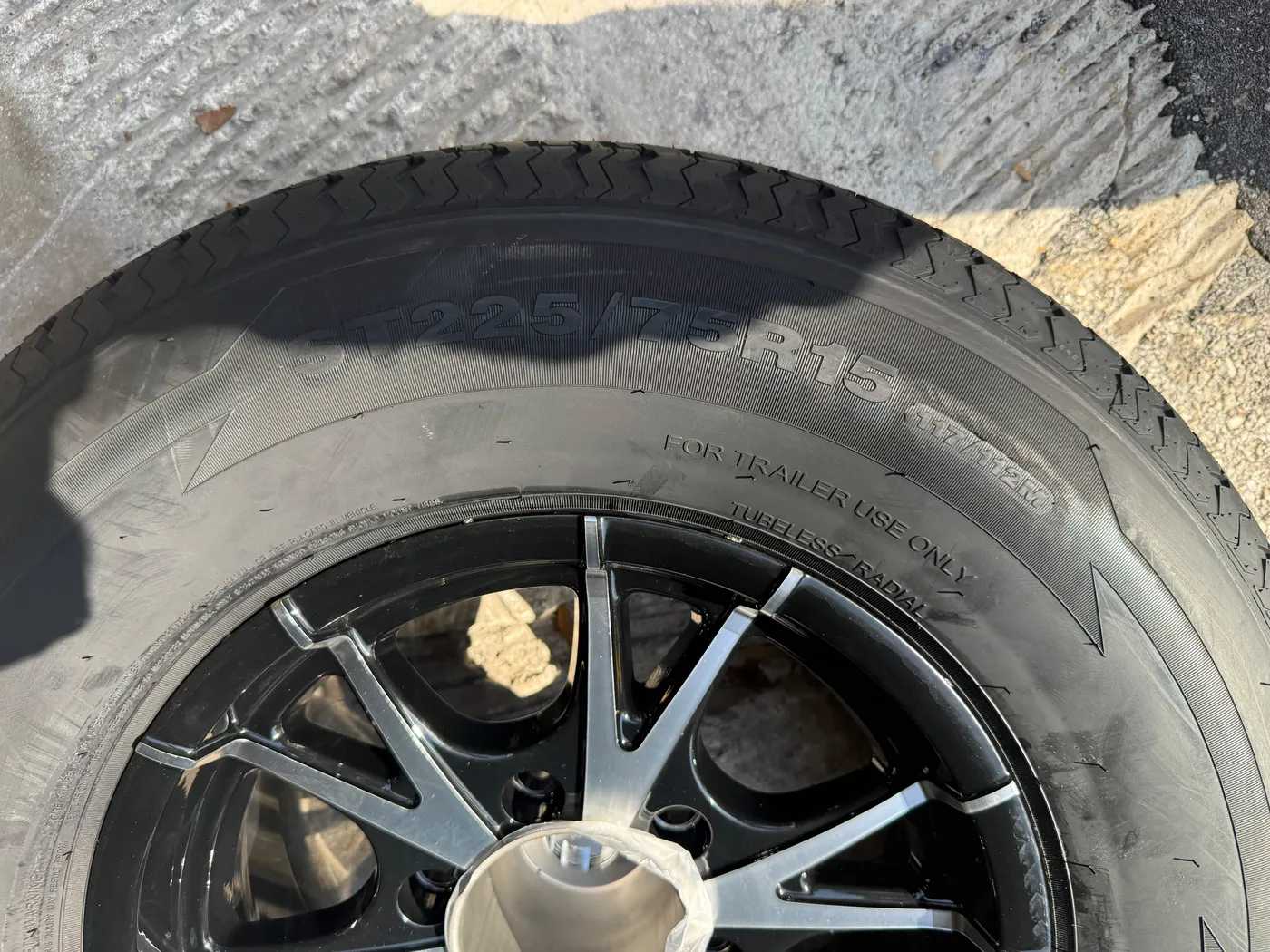ST225/75R15 trailer tire sidewall showing size and load rating on a black machined wheel